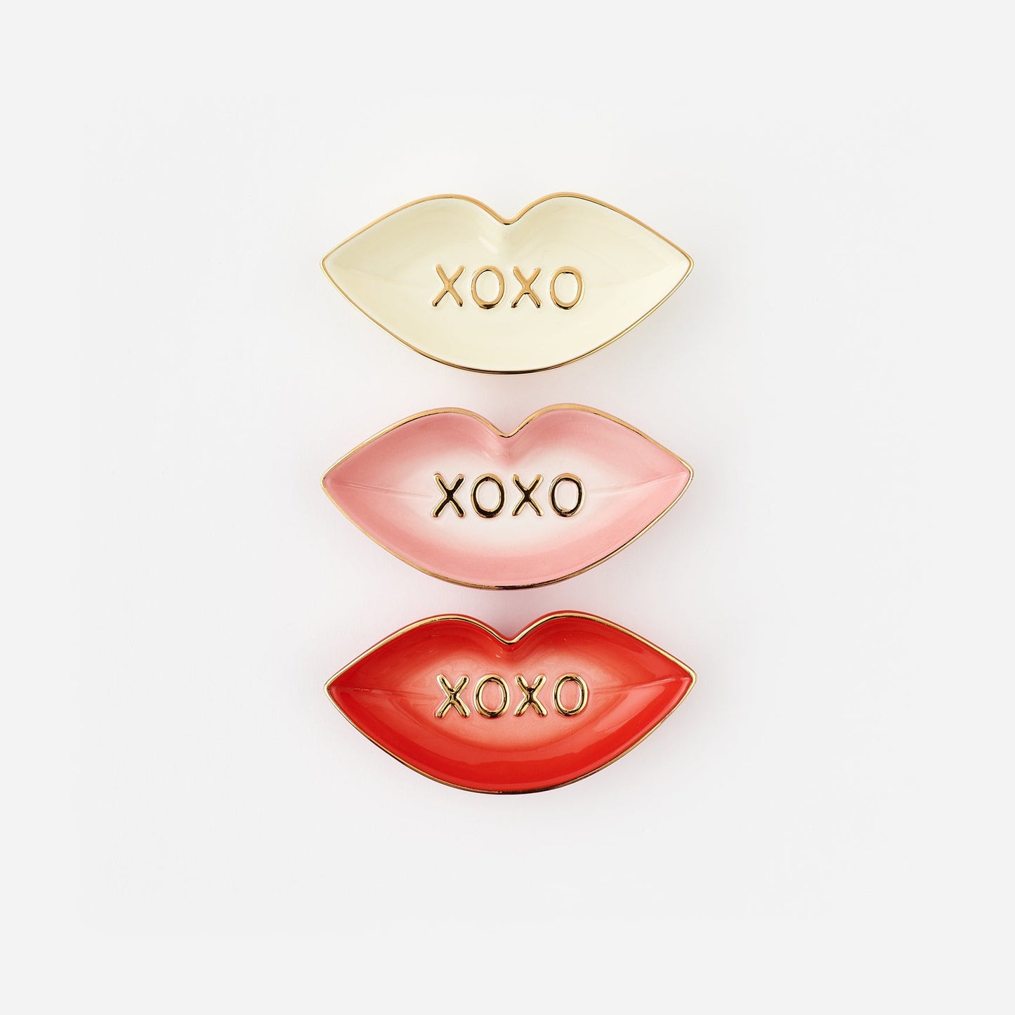 Three lip-shaped trinket dishes in gold, pink, and red with 'XOXO' text on a white background.
