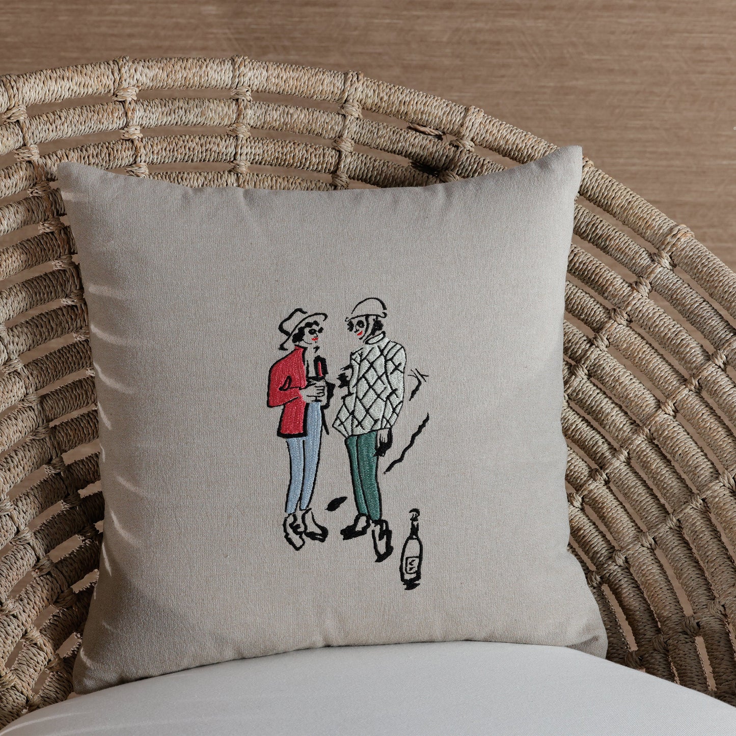 Decorative pillow with embroidered design of two people on a wicker chair.