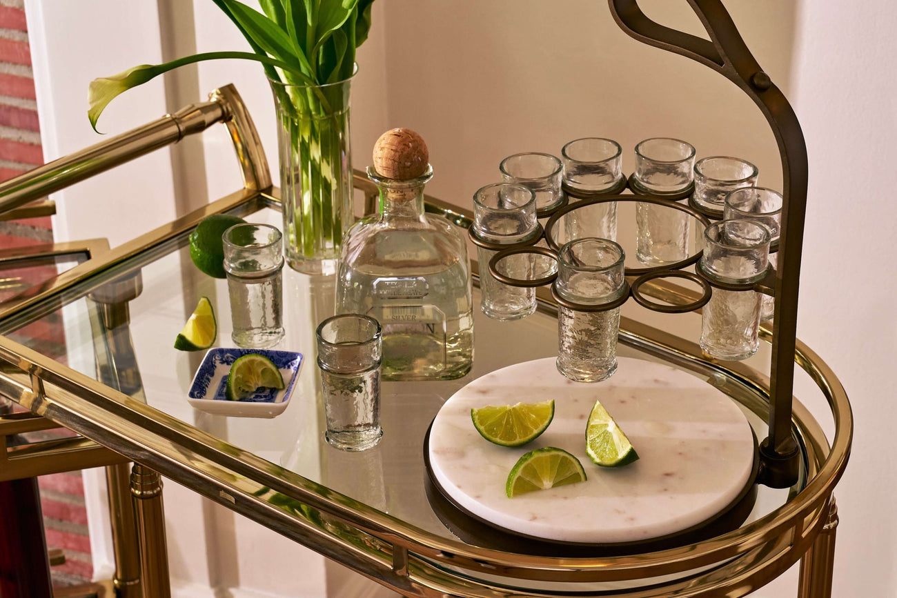 Elegant barware display with cocktail glasses, a decanter, and fresh limes on a stylish bar cart.