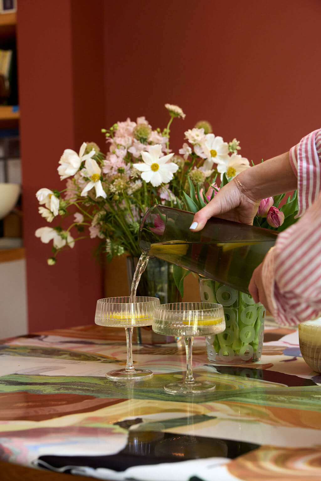 Pouring a drink into stylish glasses from the drinkware collection, featuring vibrant flowers and a colorful table.