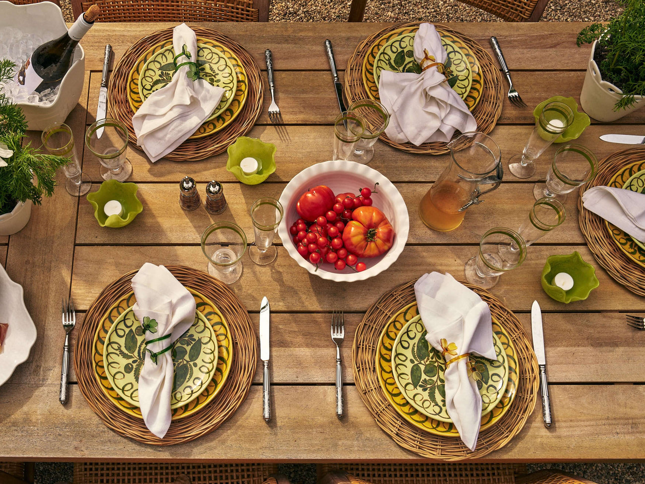 Elegant table setting featuring vibrant tableware with decorative plates, glasses, and tomatoes.