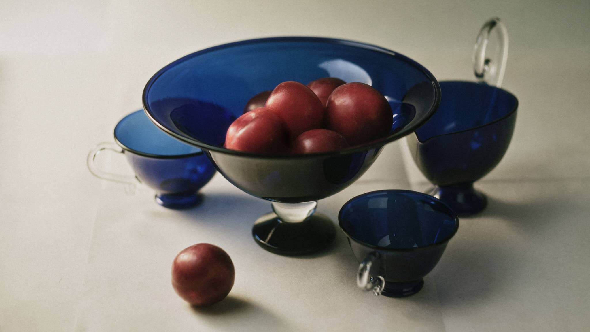 Fruit Bowl, Blue/Clear filled with red plums, showcasing elegant glass design with matching cups.