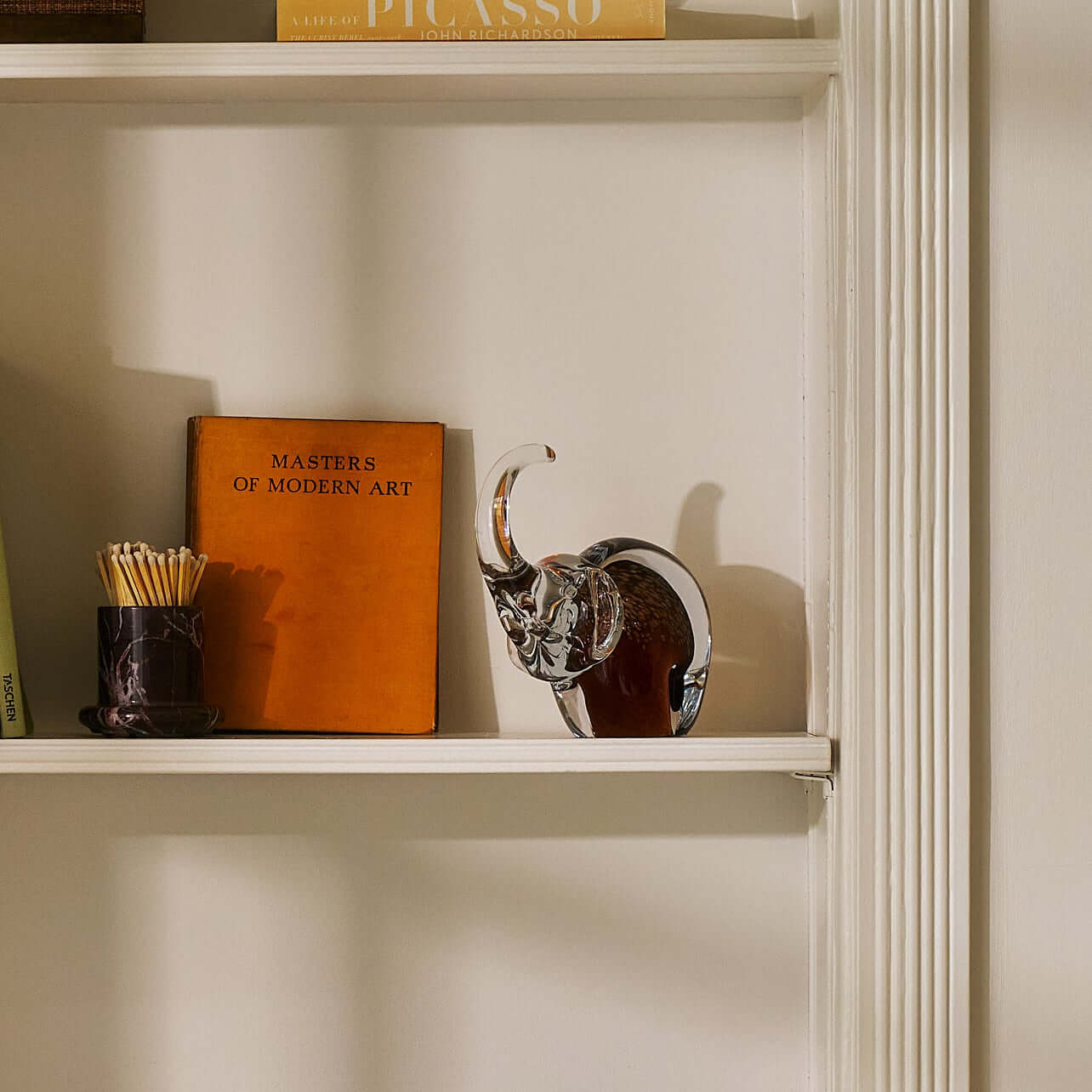Great Elephant - Golden Amber Glass sculpture displayed on a bookshelf alongside art books.