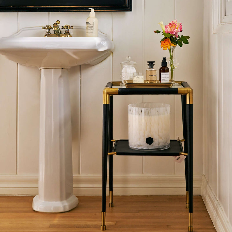 Peninsula Leather Side Table with brass joints, glass top, and black leather, styled with decor and a sink in the background.