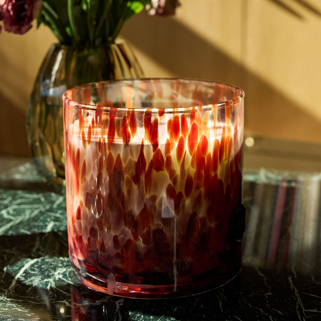 Decorative glass candle with a floral arrangement in the background