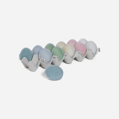 Pastel-colored pom-poms in a cardboard egg carton on a white background