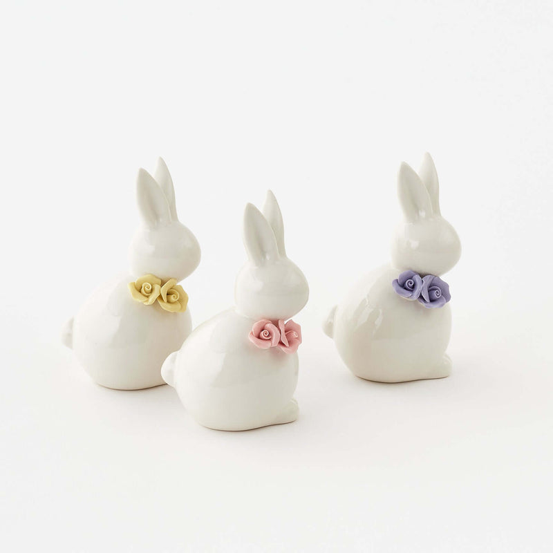 Three white ceramic bunny figurines with colorful flower collars on a white background