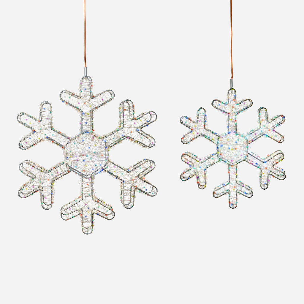 Two hanging snowflake ornaments made of iridescent glittery material, shown on a plain light gray background.