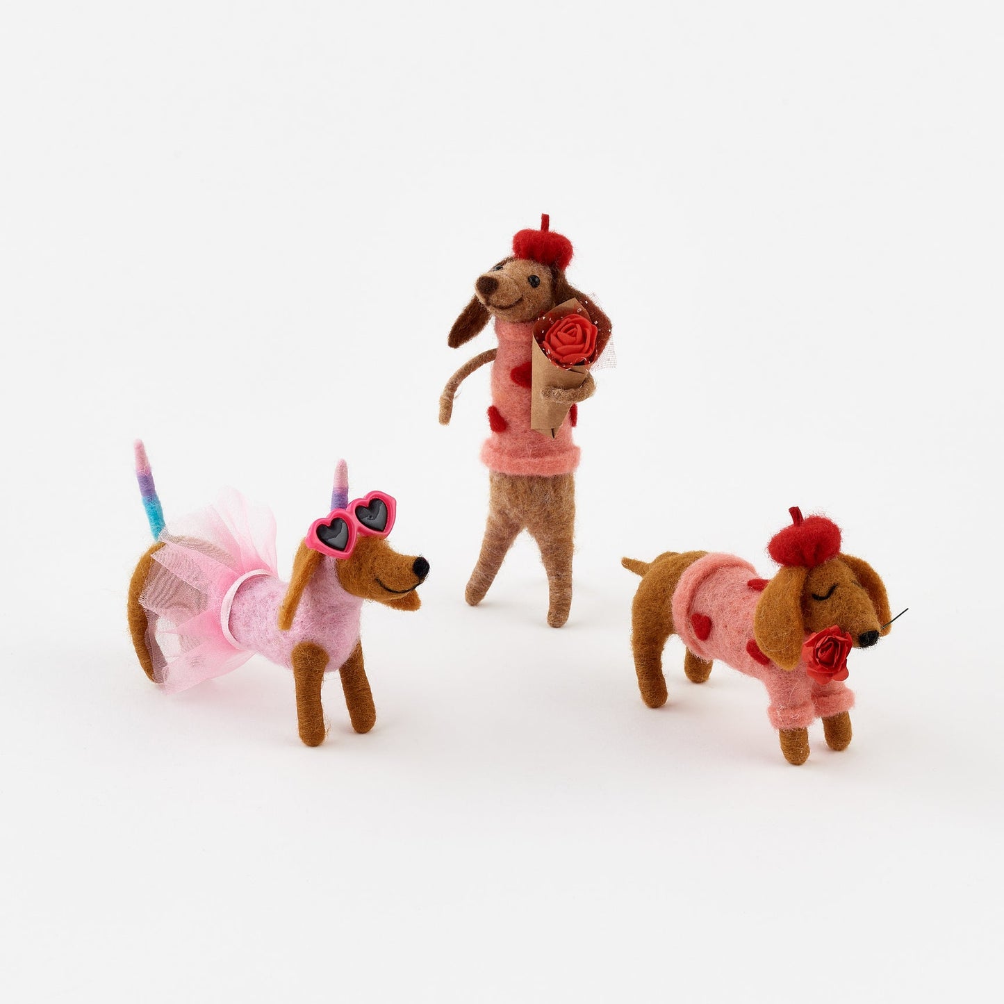 Three dog-shaped toys in pink outfits with accessories on a white background