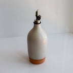 Tall Handmade Ceramic Oil Bottle in matte white with polished pourer and terracotta base on a counter.