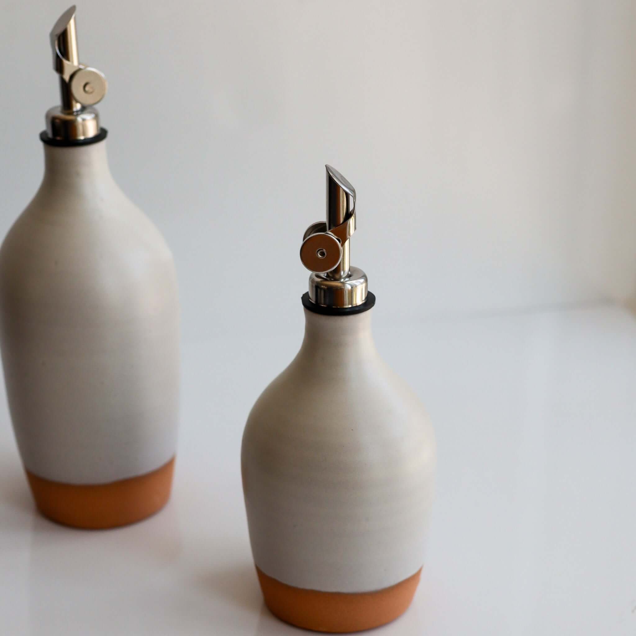 Handmade Ceramic Oil Bottle in matte white glaze with polished chrome pourer and unglazed terracotta foot.