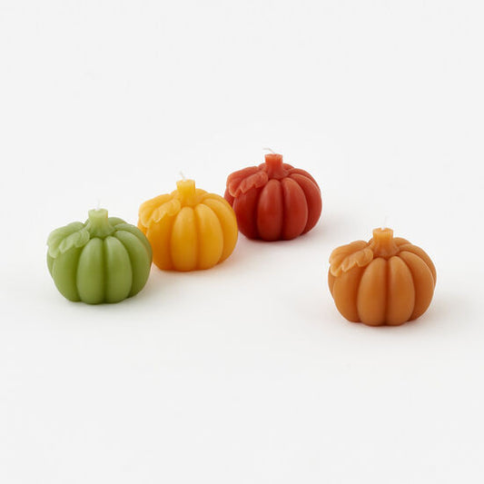 Four small pumpkin-shaped candles in green, yellow, orange, and red on a white background