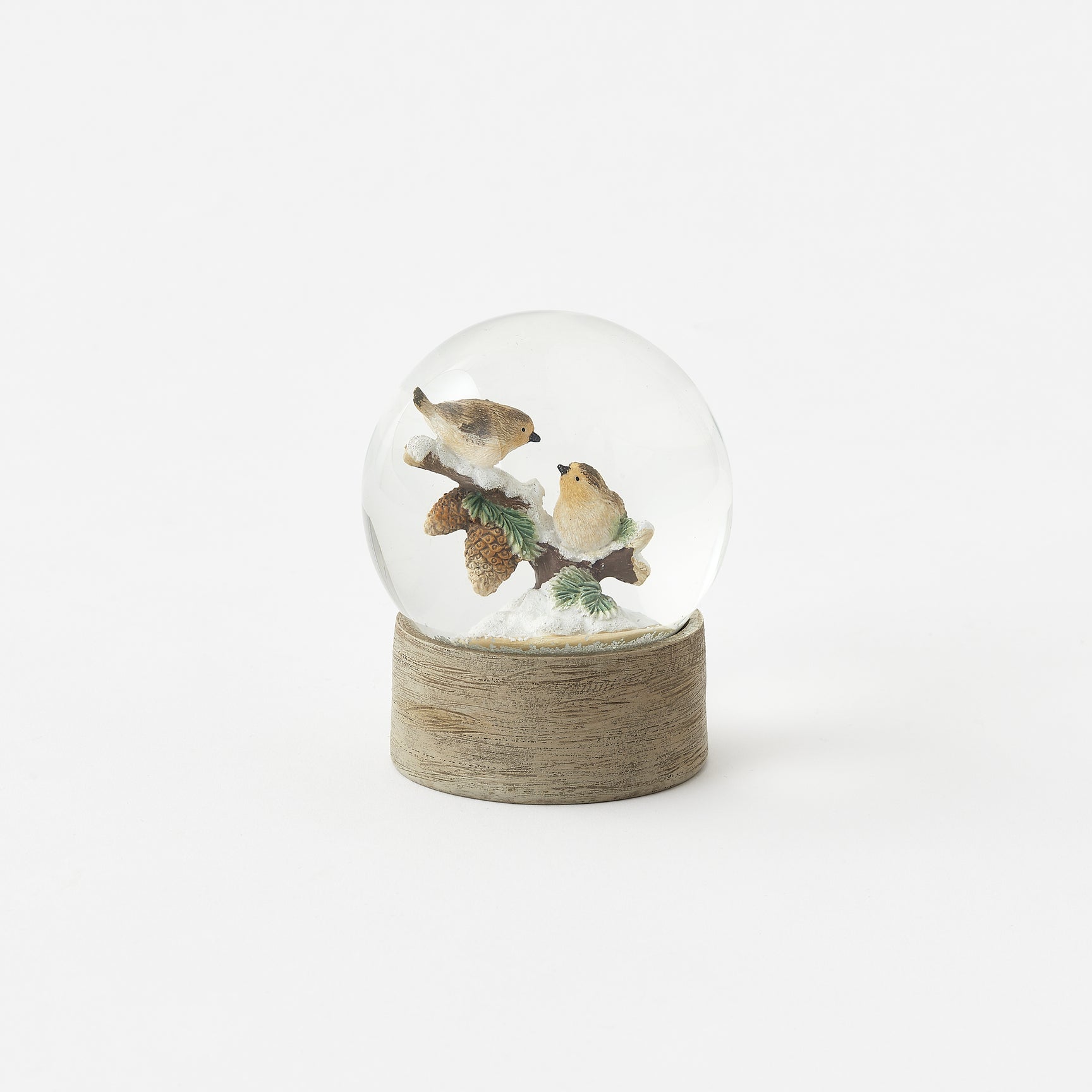 Snow globe with birds on a branch inside, placed on a wooden base against a white background