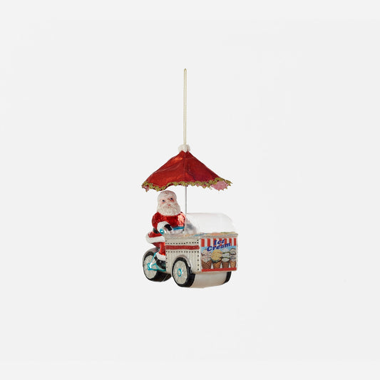 Decorative ornament of Santa Claus on an ice cream cart with a red umbrella on a white background.