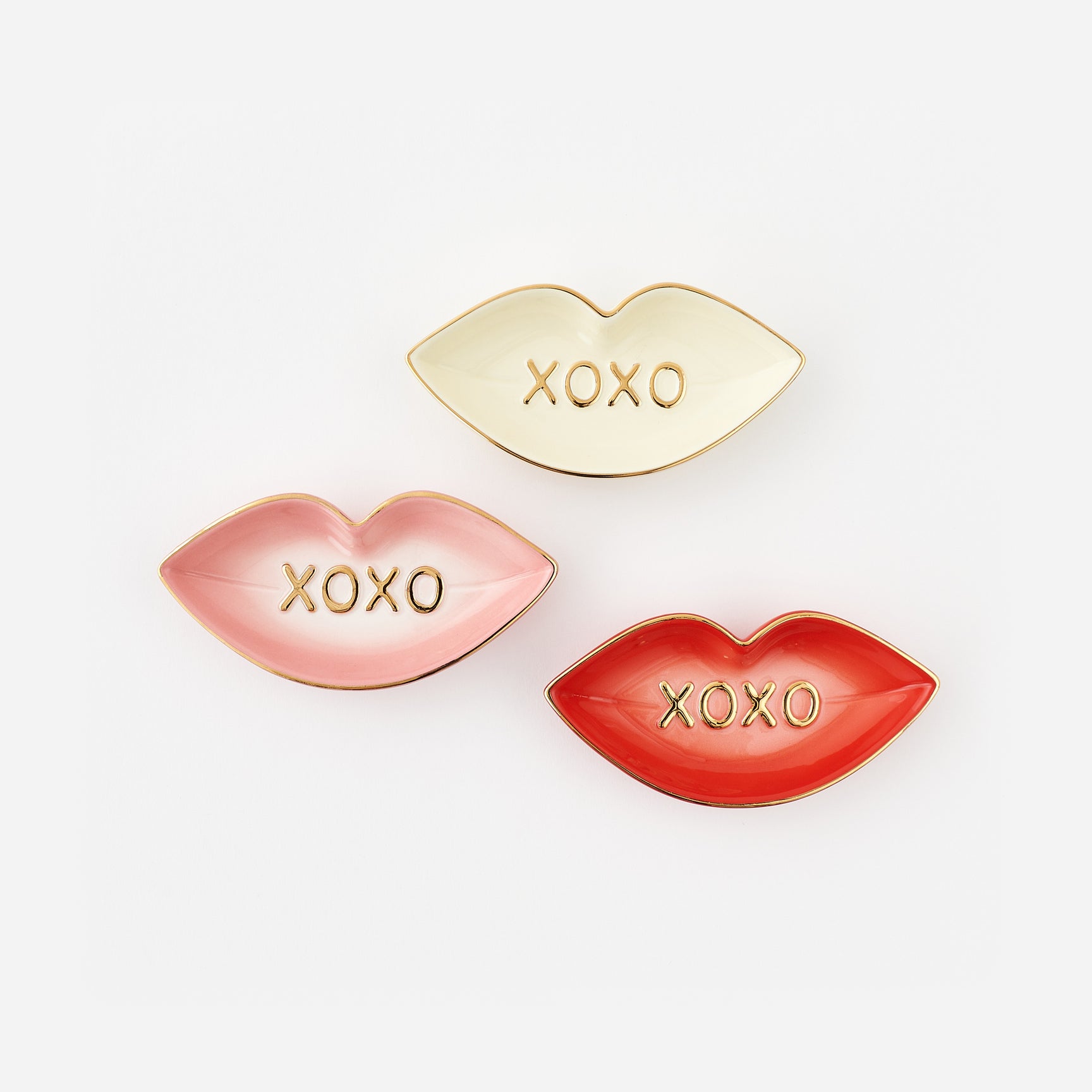 Three lip-shaped trinket dishes in gold, pink, and red with 'XOXO' text on a white background.