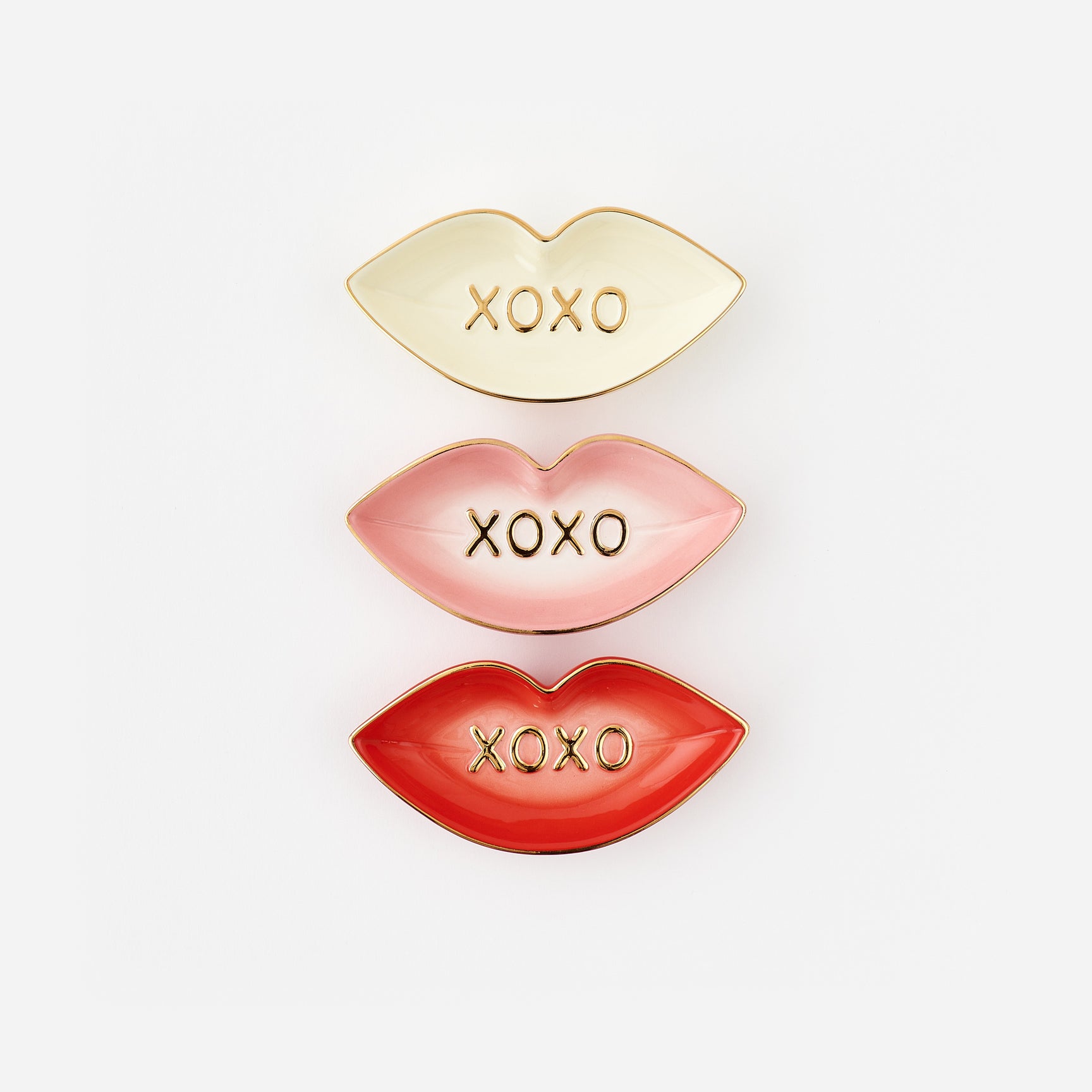 Three lip-shaped trinket dishes in gold, pink, and red with 'XOXO' text on a white background.
