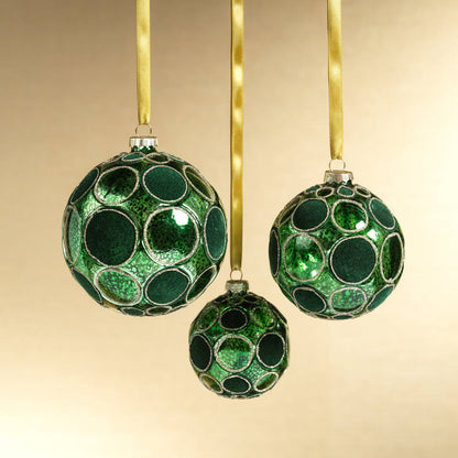 Three green decorative balls with gold ribbons on a beige background