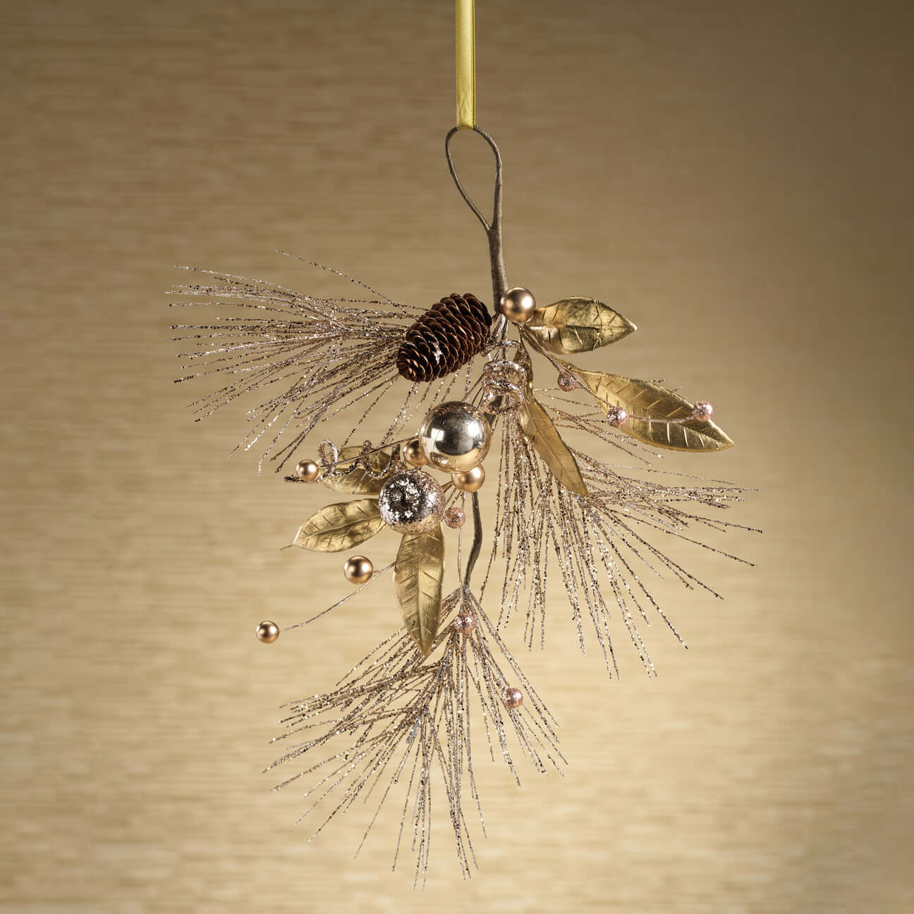 Decorative ornament with gold leaves, pinecones, and beads on a beige background