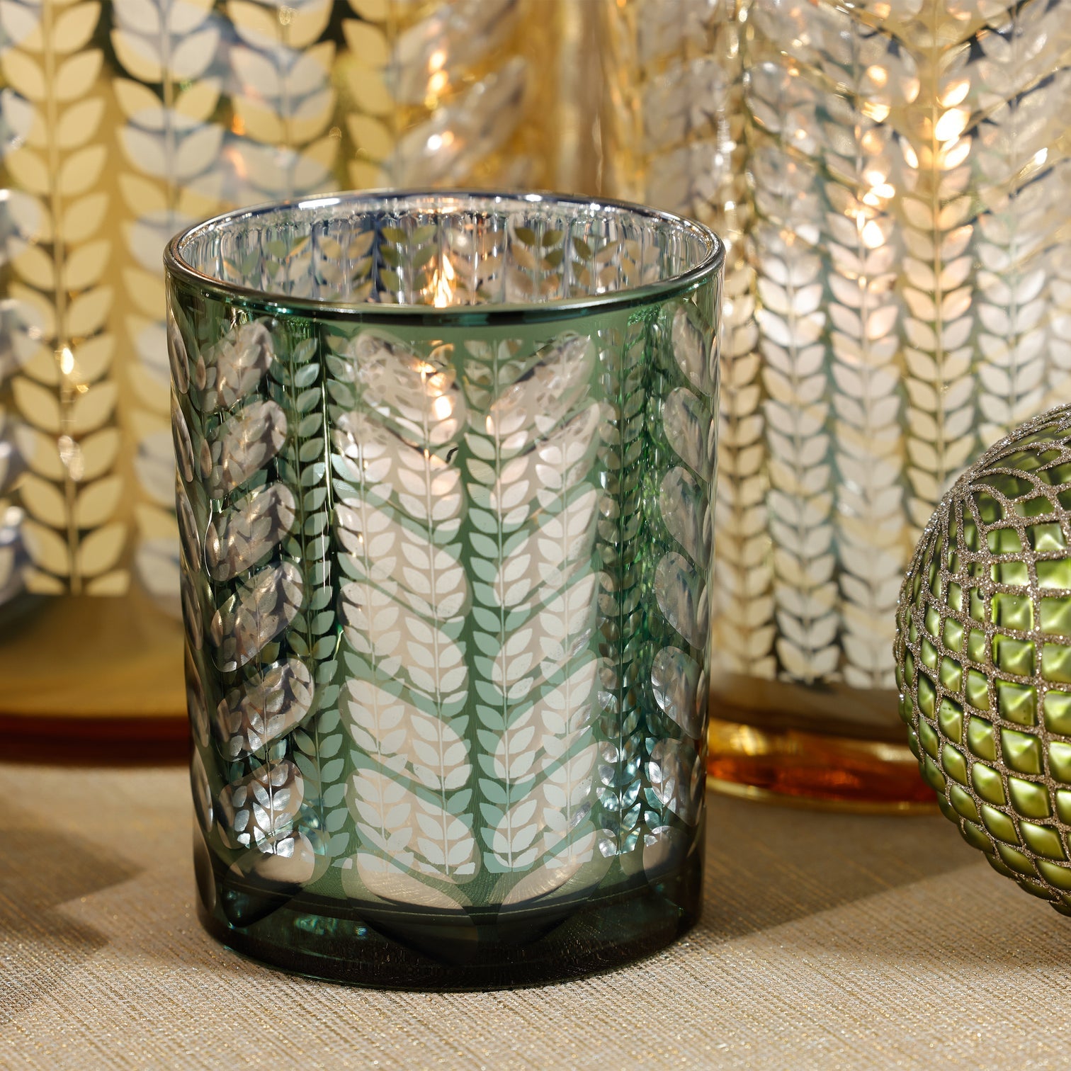 Decorative glass candle holder with leaf pattern on a textured surface
