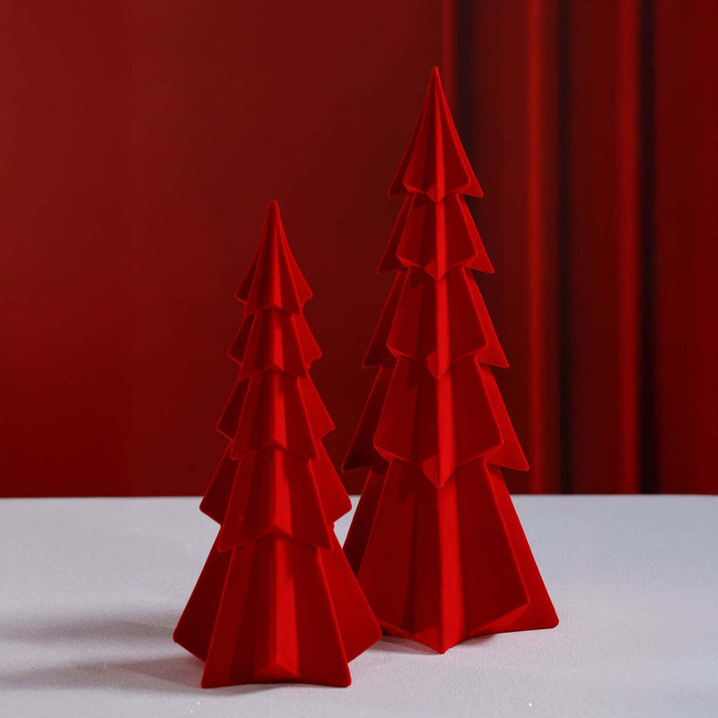 Two red, tiered Christmas tree decorations against a red curtain.