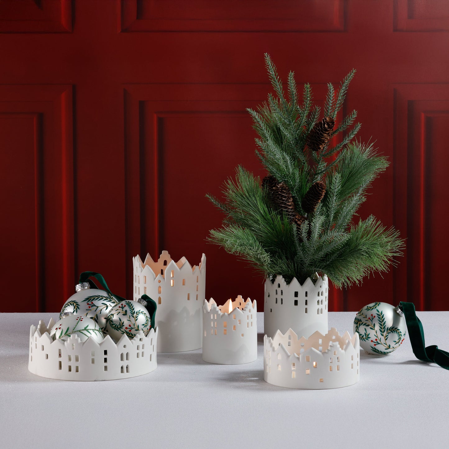 Decorative white candle holders with greenery against a red wall