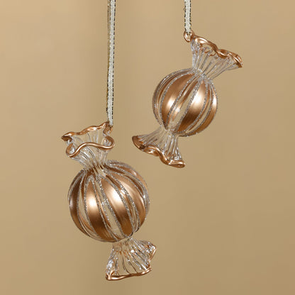 Two gold and clear candy-shaped ornaments on a beige background