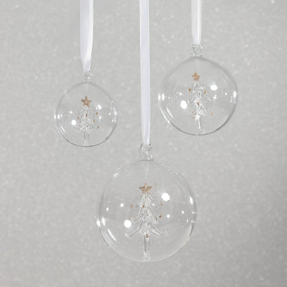 Three clear Christmas ball ornaments with tree designs on a gray background