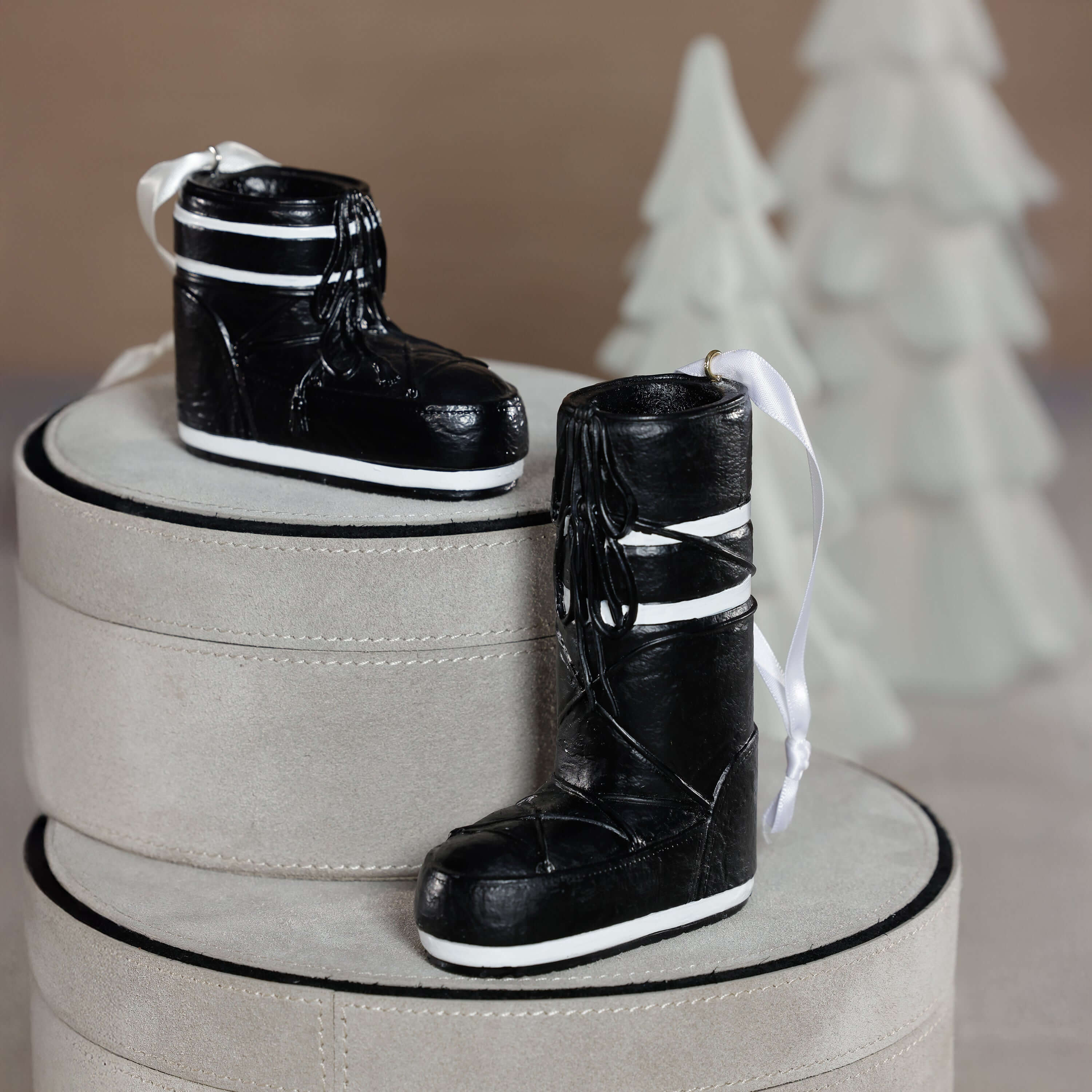 Après Ski Boots, Set of 6 Assorted black ornament displayed on grey boxes with decorative trees in the background.