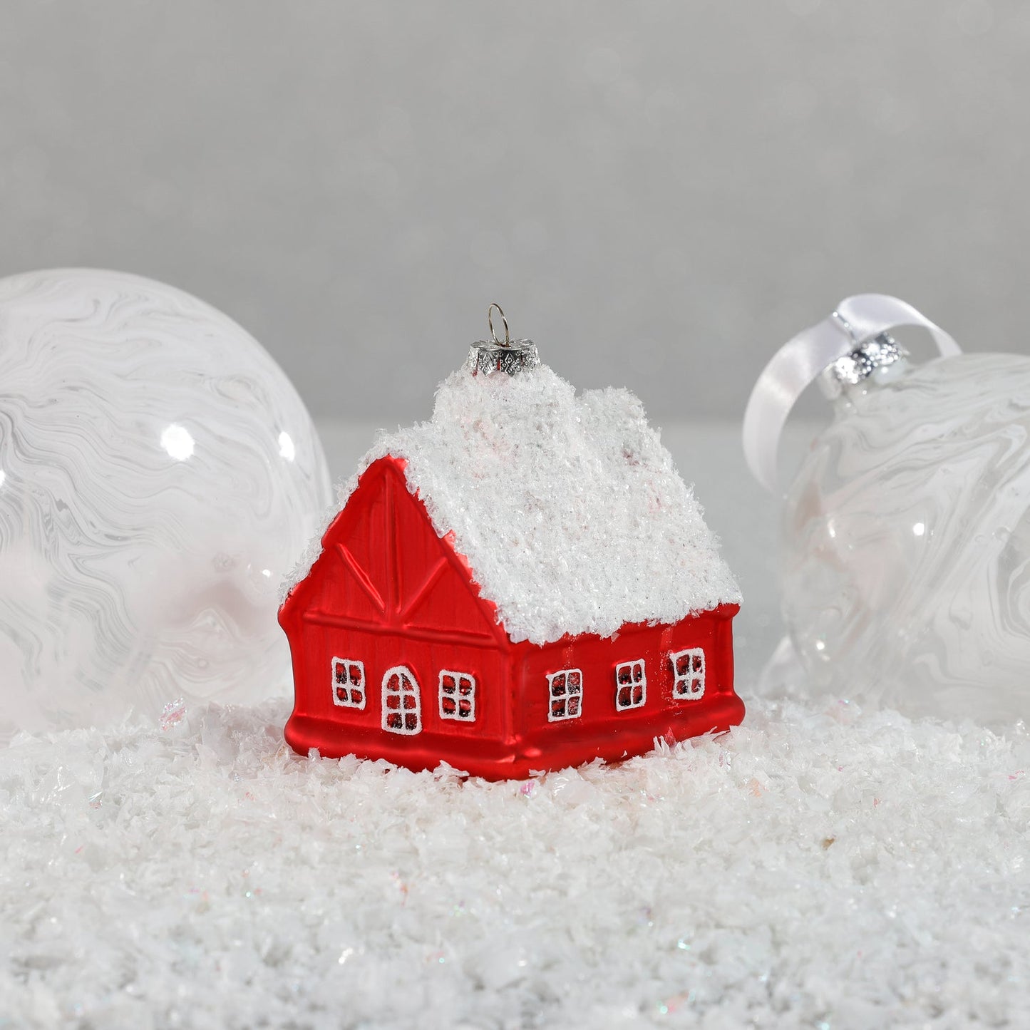 Red house ornament with snow on top on a gray background