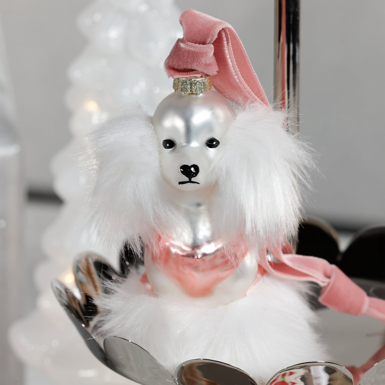 Decorative dog ornament with a pink bow and silver outfit on a white background