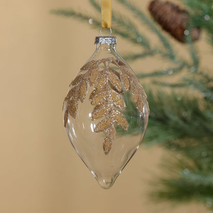 Clear glass ornament with gold leaf design hanging on a tree.