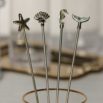 Four decorative stir sticks with starfish, shell, seahorse, and whale tail ends on a stand.