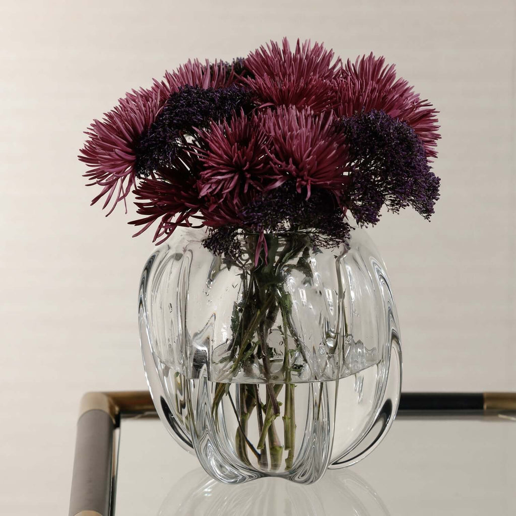 Liège Blown Glass Vase filled with vibrant purple flowers, showcasing its sculptural design and clear glass craftsmanship.