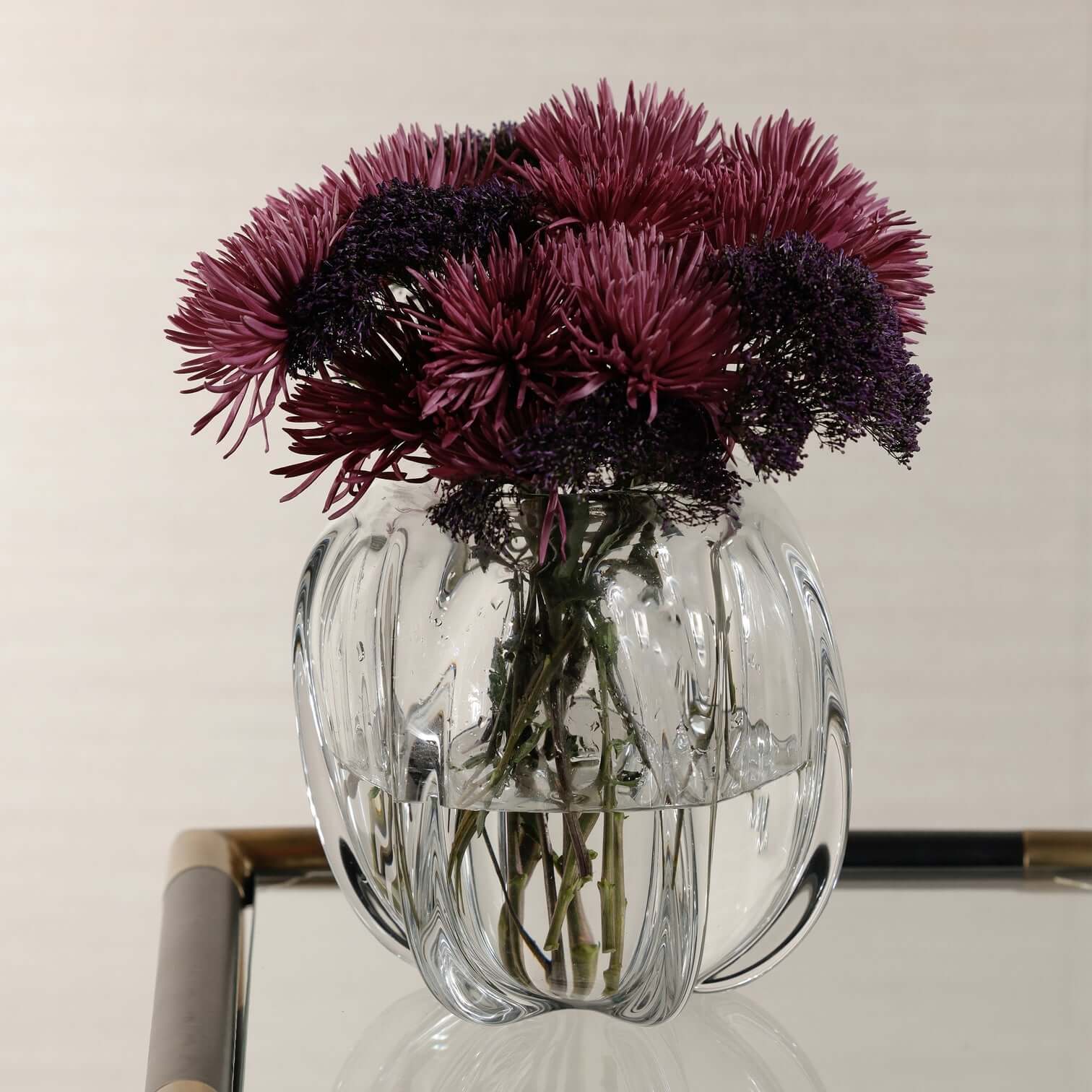 Liège Blown Glass Vase filled with vibrant purple flowers, showcasing its sculptural design and clear glass craftsmanship.