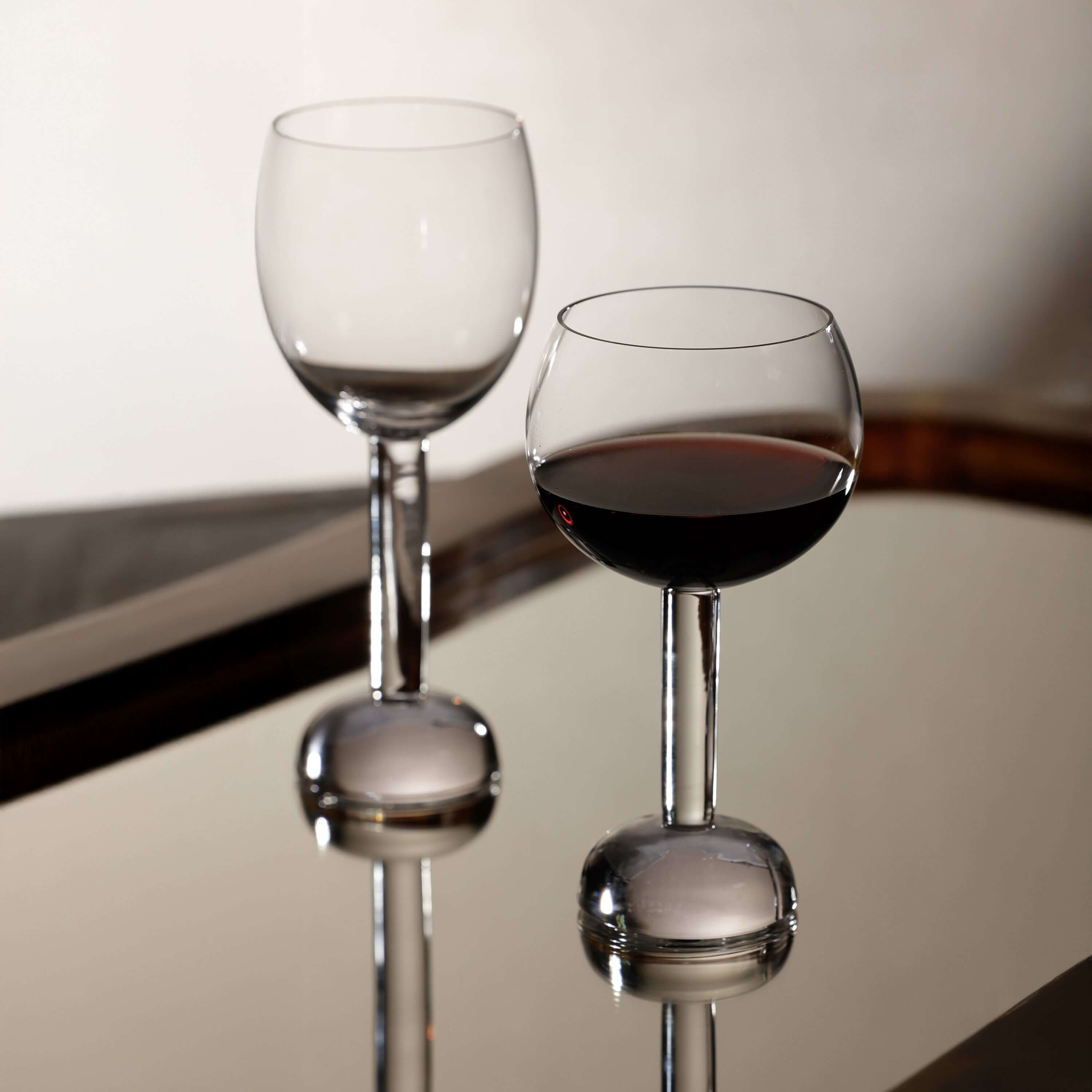 Madrid Glassware Collection featuring two elegant glasses with a sculptural sphere base and contrasting drinks.