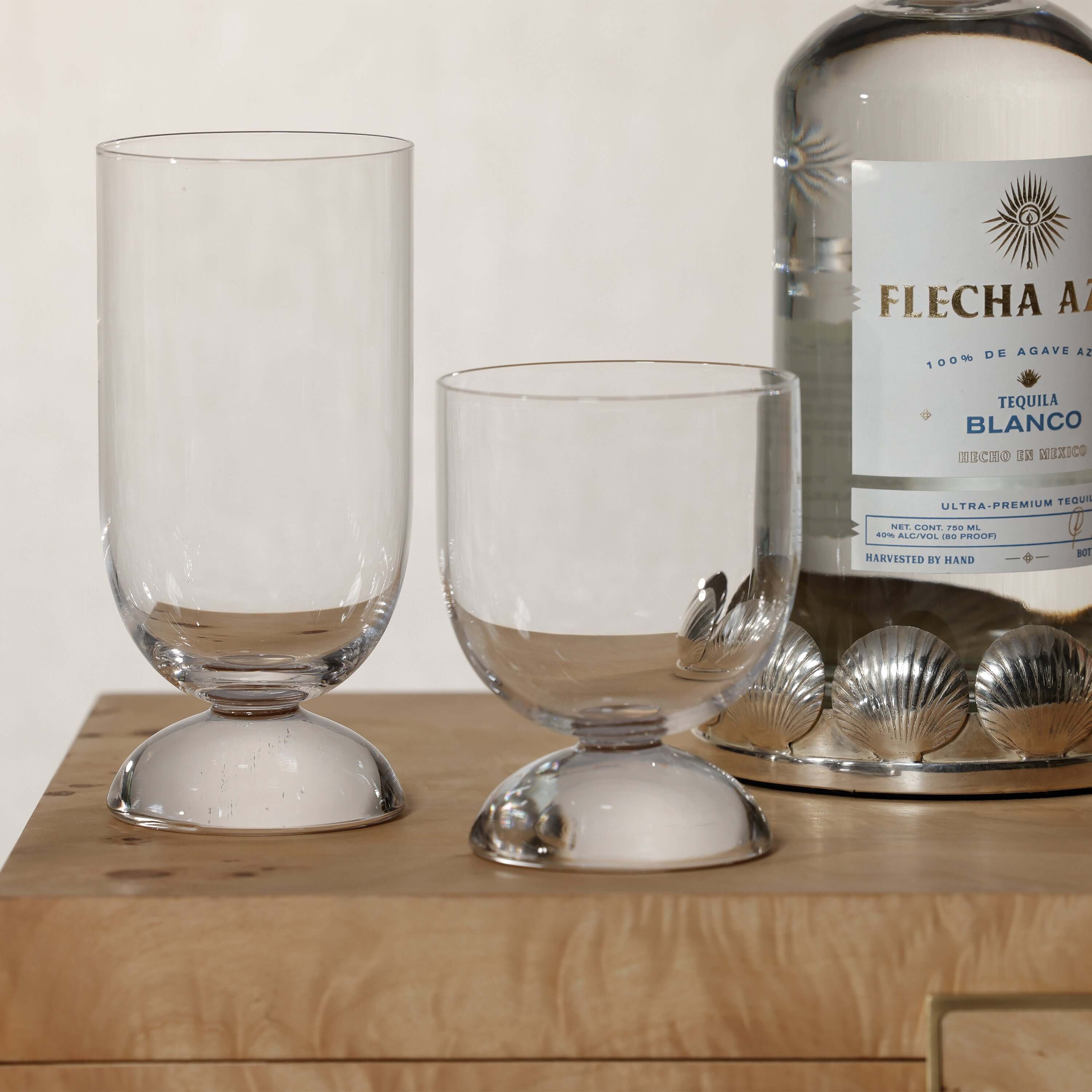 Madrid Glassware Collection displayed with two elegant glasses and a bottle of tequila on a wooden surface.