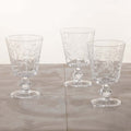 Three clear glass goblets with intricate designs on a light wooden surface.