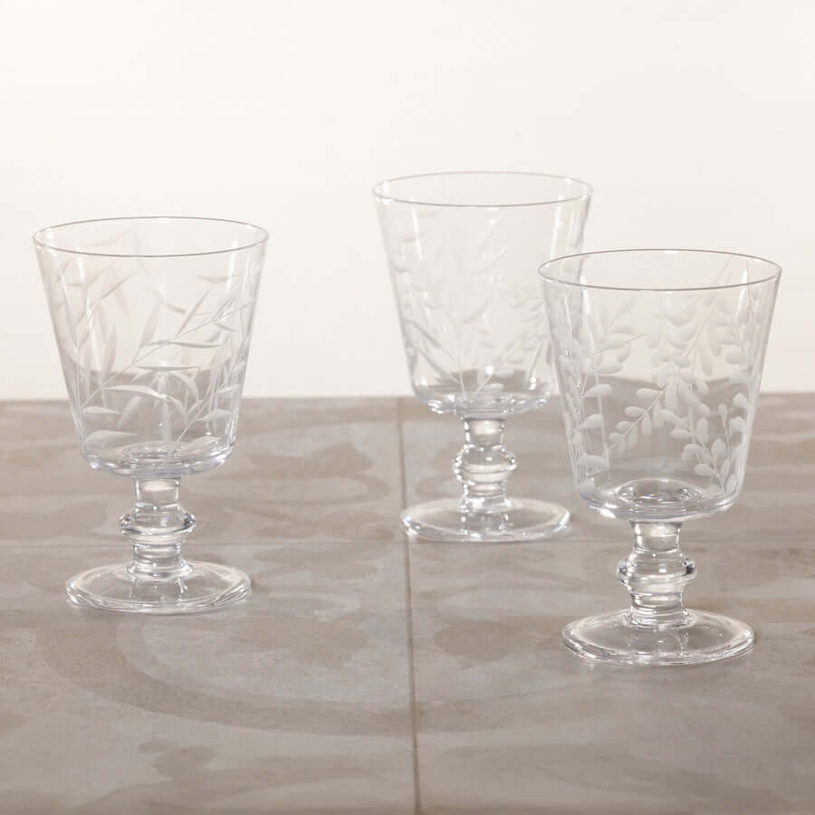 Three clear glass goblets with intricate designs on a light wooden surface.