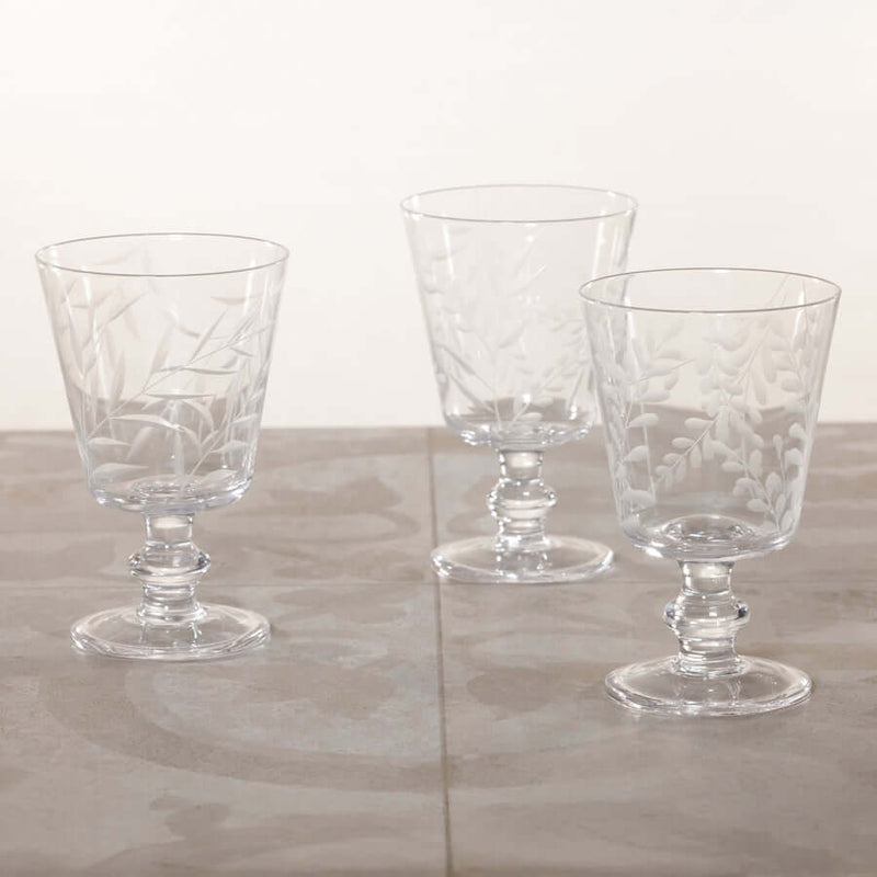 Three clear glass goblets with intricate designs on a light wooden surface.