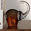 Great Elephant - Golden Amber Glass sculpture on wooden table next to a book, showcasing its elegant design.