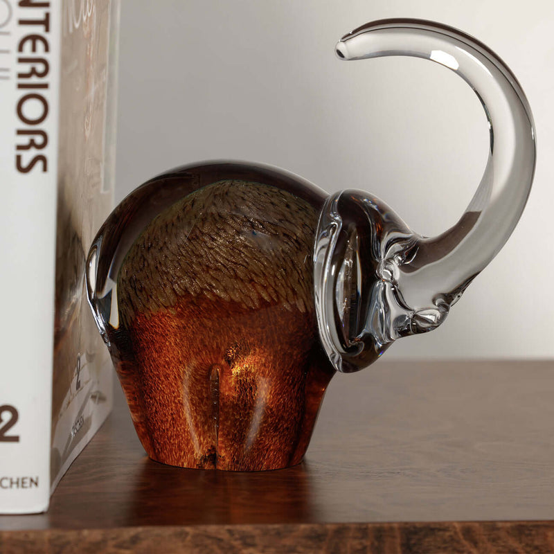 Great Elephant - Golden Amber Glass sculpture on wooden table next to a book, showcasing its elegant design.
