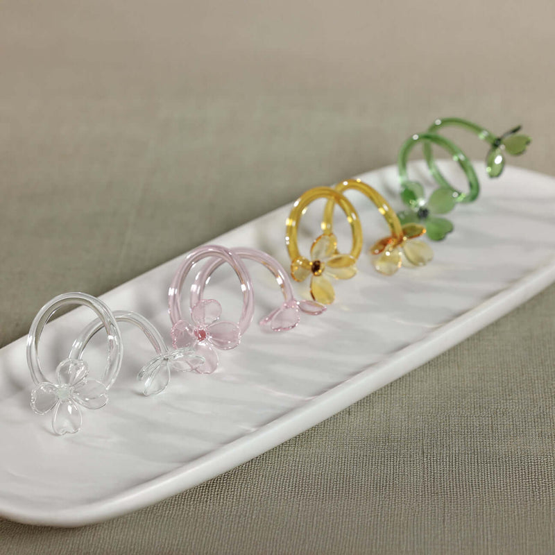 Four Botanica Glass Flower Napkin Rings - Boxed (Set of 4) displayed on a white plate with pastel colors.