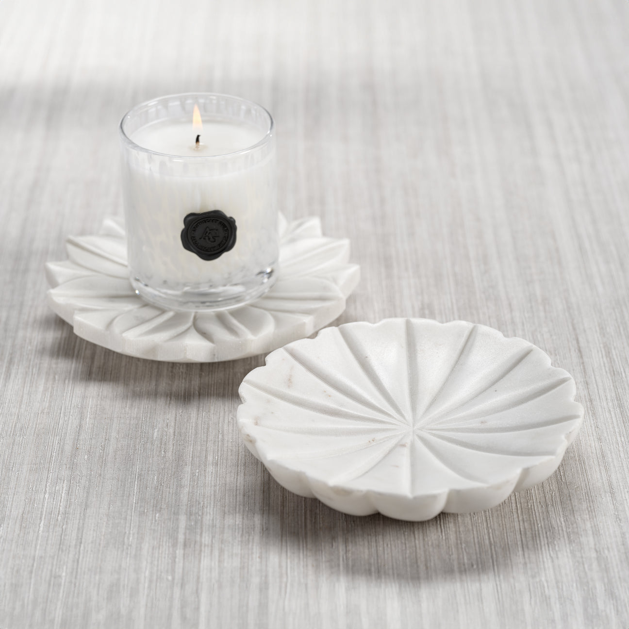 White decorative candle holder with a small candle on a light gray surface