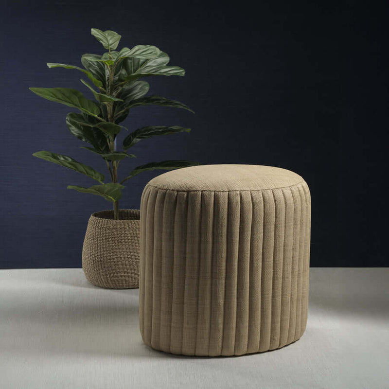 Fontainebleau Oval Fluted Raffia Ottoman with natural texture and tailored fluting alongside a decorative plant.