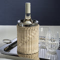The Palmier Wine Cooler with handwoven rattan exterior and polished metal interior, holding a bottle of white wine on a tray beside glasses.