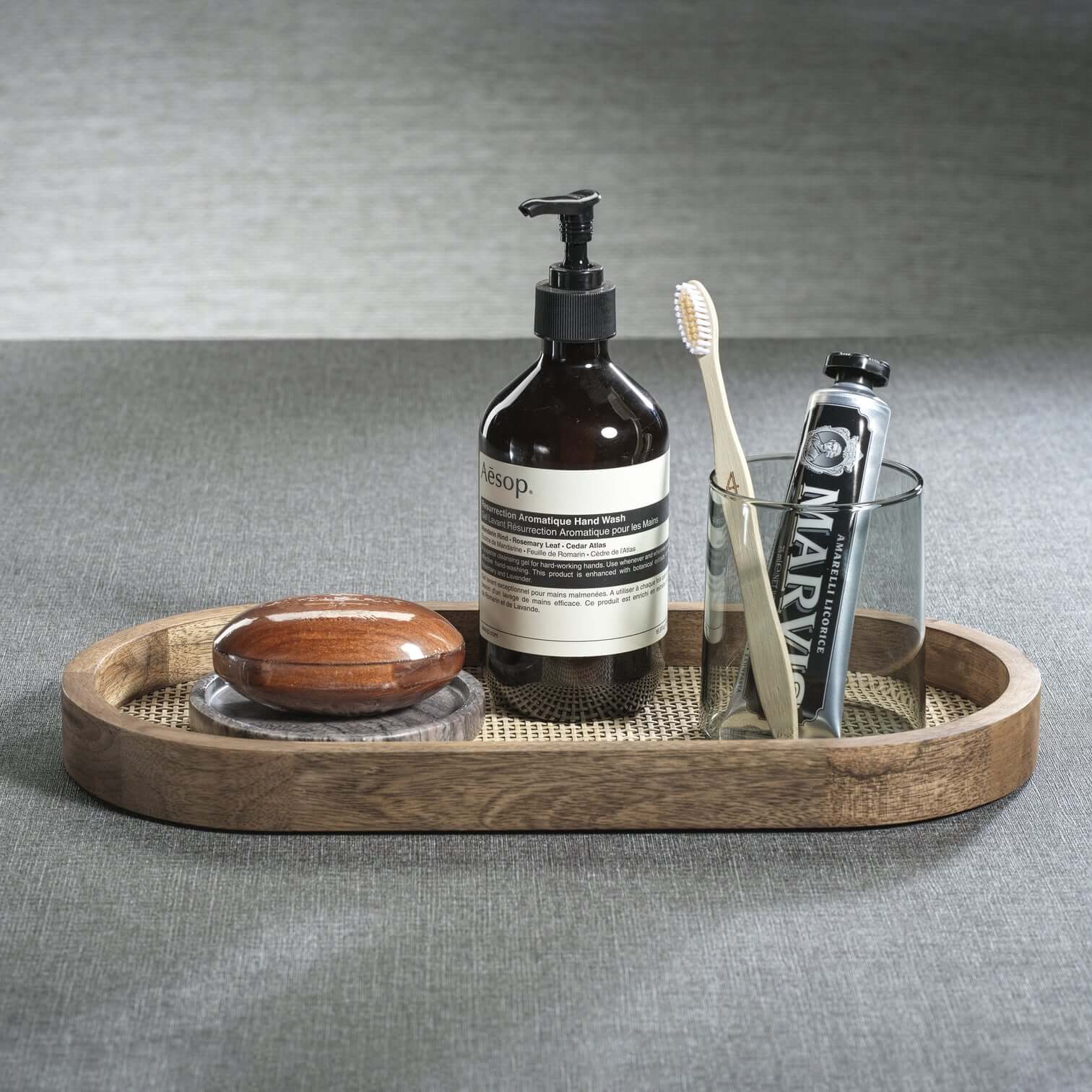 The Marais Oval Tray displaying a stylish arrangement of hand wash, toothbrush, and soap on a textured surface.