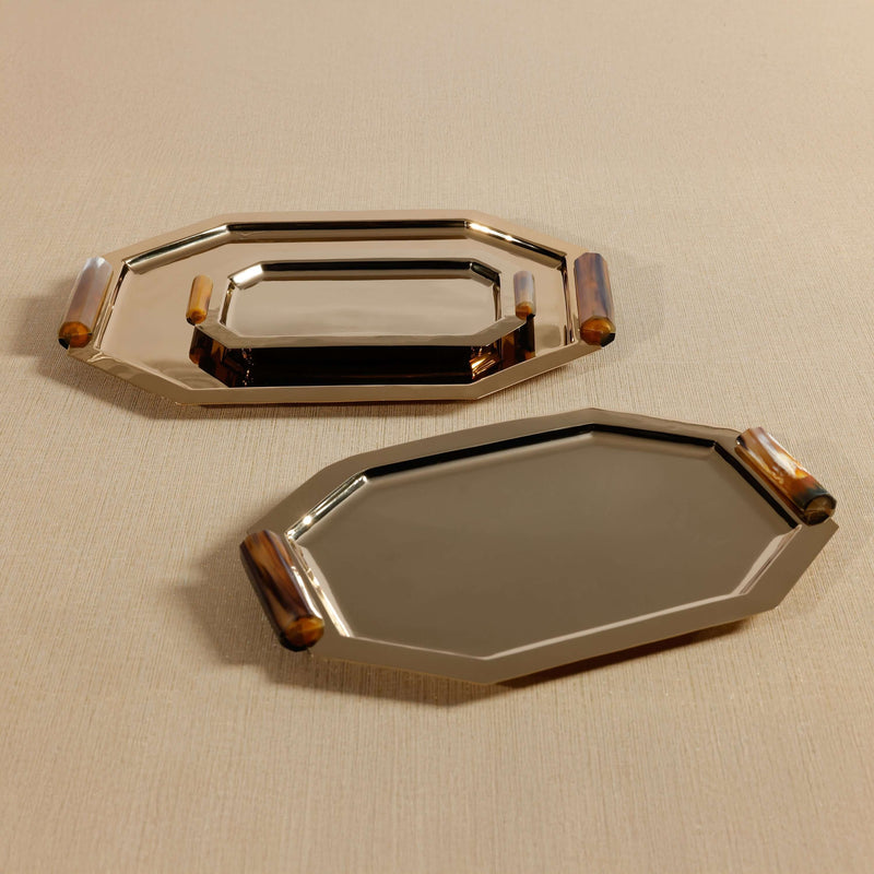 Two metallic trays with decorative handles on a beige surface