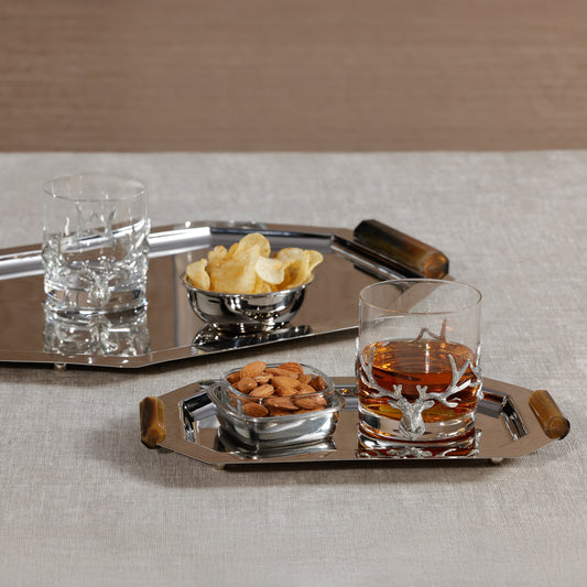 Tray with glass of whiskey, bowl of nuts, and bowl of chips on a neutral background