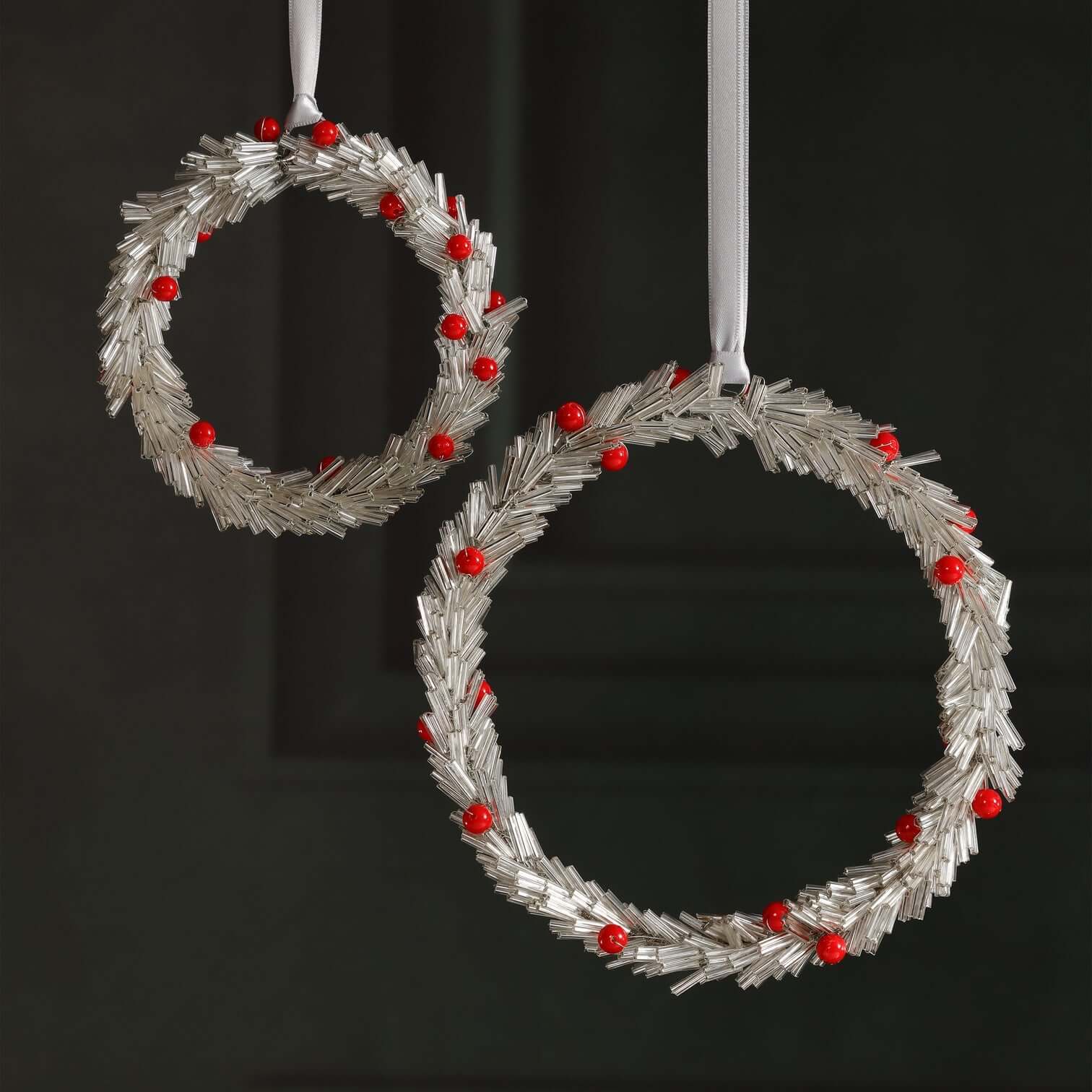 Two silver wreath ornaments with red berries on a black background