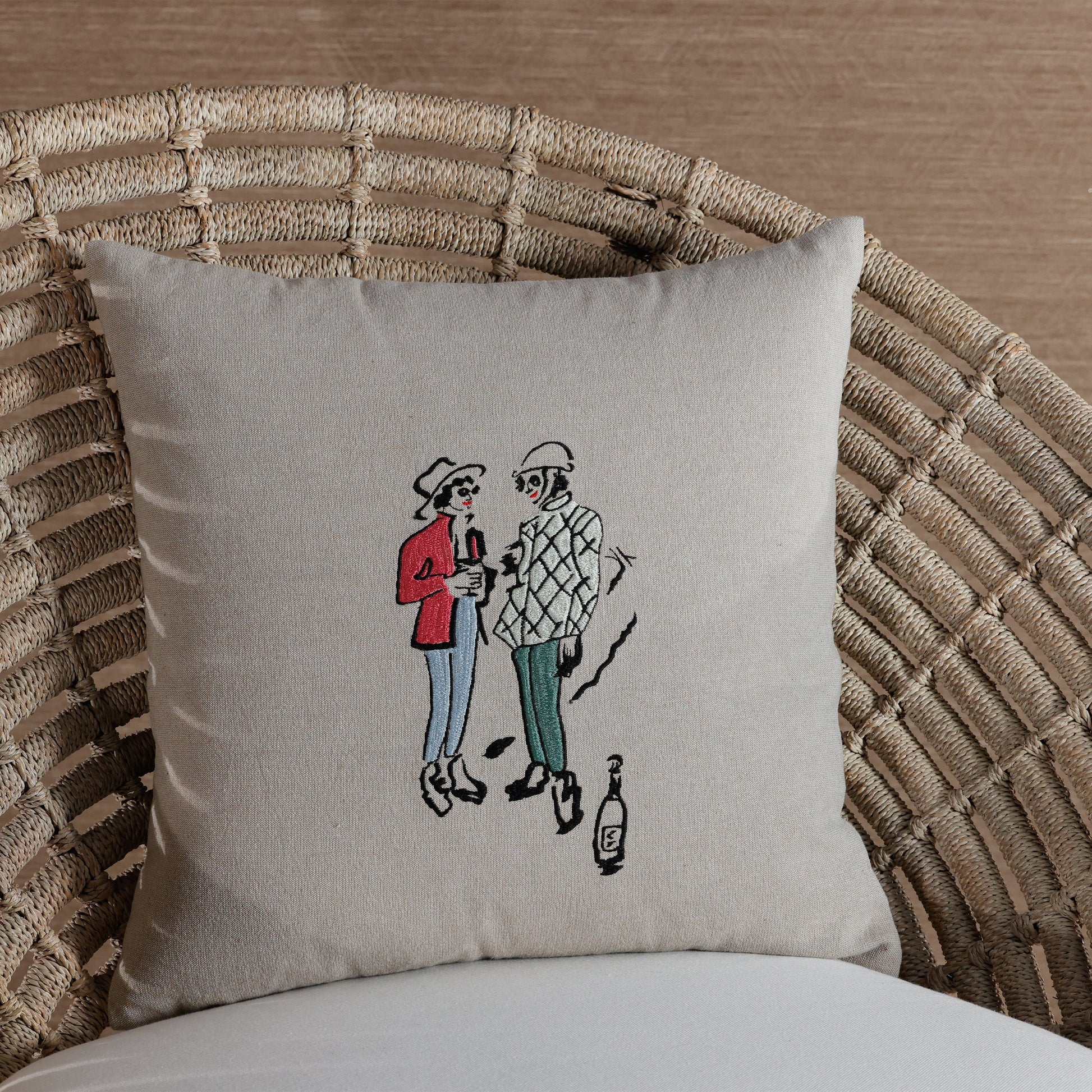 Decorative pillow with embroidered design of two people on a wicker chair.